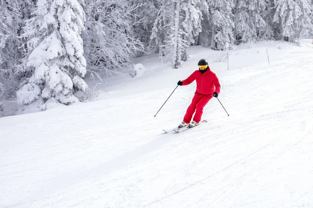 A skier in red making a turn on a snow-covered mountain piste